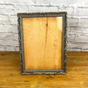 May include: A silver picture frame with an ornate design. The frame is empty and has a glass front.