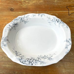 May include: Oval white serving dish with a scalloped edge, decorated with a floral pattern in shades of grey and blue. The dish has a smooth, glossy surface, likely made of ceramic or porcelain.