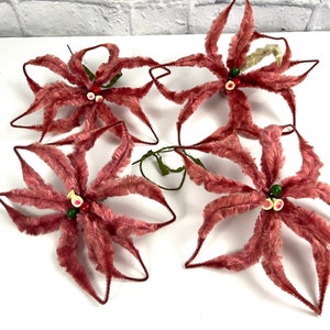 Peut inclure: Quatre décorations de Noël en poinsettia de velours rose avec des accents de perles vertes et blanches.