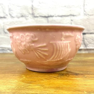 Puede incluir: Un cuenco de cerámica rosa con un diseño en relieve de un barco y flores. El cuenco es perfecto para una planta pequeña o uso decorativo.