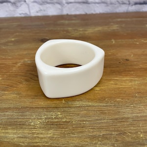 May include: A white triangular bangle bracelet made of smooth plastic.