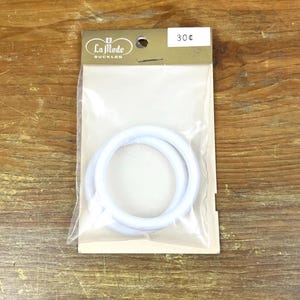 May include: A package of two white, circular La Mode buckles. The package is sealed in clear plastic and has a gold-colored header with the brand name and a price tag.