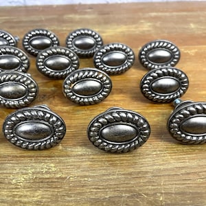 Puede incluir: Una colección de 15 pomos de armario de forma ovalada con un acabado plateado y un diseño de cuerda alrededor del borde.