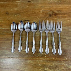 May include: A set of stainless steel silverware, including spoons and forks, arranged on a wooden surface. The spoons and forks have decorative handles. The silverware is likely for dining or serving.