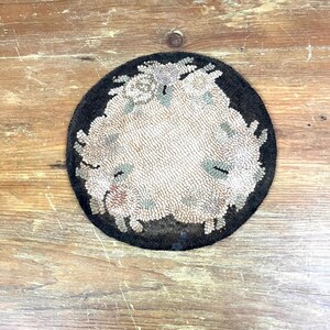 Pode incluir: Um tapete redondo de crochet preto e branco com um design floral. O tapete é feito de lã e tem uma borda franjada.
