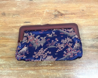 Puede incluir: Un bolso de mano de satén azul con un estampado floral rojo y dorado y un cierre de metal. El bolso tiene un diseño chino tradicional.