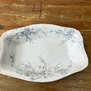 May include: White rectangular serving dish with a floral design in grey. The dish has a slightly scalloped edge and is set against a wooden surface. The number "4" is written in black marker in the upper left corner.