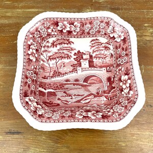 May include: A square, antique-style serving dish with a red and white landscape design. The dish features a bridge, trees, and a castle. The rim is decorated with floral patterns.