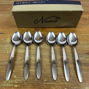 Puede incluir: Seis cucharas de plata en fila sobre una superficie de madera. Las cucharas son todas del mismo tamaño y forma, y tienen un diseño simple y elegante. Las cucharas están en una caja que dice "Lifetime Stainless Nasco".