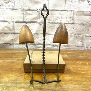 May include: A vintage shoe stretcher with two wooden forms and a twisted metal handle. The shoe stretchers are mounted on metal rods and are designed to expand the width and length of shoes. The word "MINIATURES" is visible on the box behind the shoe stretcher.