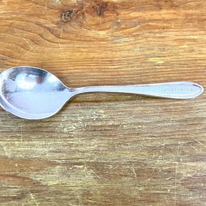 May include: A silver spoon with a rounded bowl and a long handle. The handle is engraved with the words "Taunton Inn".