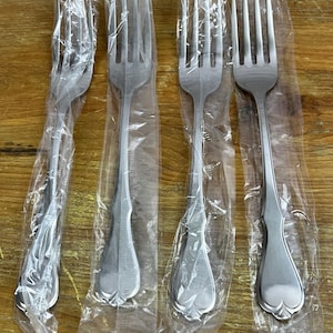 May include: Four silver forks individually packaged in plastic. The forks feature an ornate design at the top of the handle.