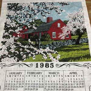 May include: A vintage 1985 calendar tea towel featuring a red farmhouse with white blossoms in the foreground. The calendar shows the months of January through August.