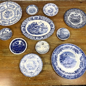 May include: A collection of blue and white ceramic plates with floral and geometric designs. The plates are arranged on a wooden surface.