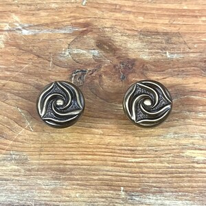 May include: Two antique brass cabinet knobs with a swirling design. The knobs have a circular shape and a raised center.