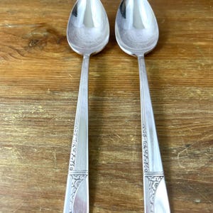 May include: A white ceramic mug with a black handle and the text "But First, Coffee" in a bold, black font. The mug is set against a blurred background, suggesting a cozy setting.