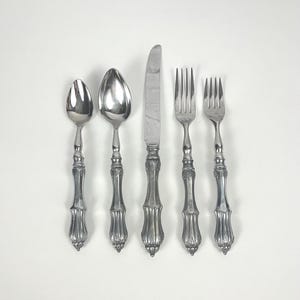 May include: A set of five silver-plated utensils, including a knife, two forks, and two spoons. The utensils have ornate, detailed handles.