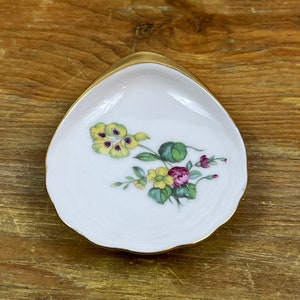 Puede incluir: Un pequeño plato ovalado blanco con un borde dorado. El plato tiene un diseño floral con flores amarillas, moradas y rojas.