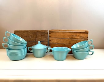 May include: A set of light blue vintage ceramic teacups and saucers with a matching creamer and sugar bowl. The set is arranged on a white surface with two wooden crates in the background.