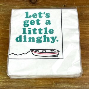 Peut inclure: Serviette en papier blanche avec un motif vert et blanc. La serviette représente un petit bateau et le texte "Let's get a little dinghy."