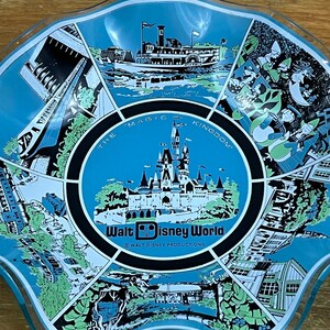 Puede incluir: Un plato para servir transparente con borde festoneado y un interior azul claro con ilustraciones de las atracciones de Walt Disney World. El centro tiene una imagen de castillo con el texto "The Magic Kingdom" y "Walt Disney World".