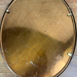 May include: The back of a round, oval-shaped, gold-colored metal picture frame with a smooth surface. The frame has four small, metal hooks on the back.