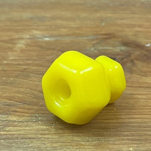 May include: Two bright yellow, geometric-shaped objects with rounded edges. One has a central hole. The objects are on a wooden surface.