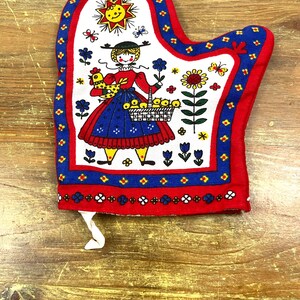 May include: Red, blue, and white oven mitt with a folk art design featuring a girl holding a basket of yellow eggs and a rooster. The design also includes a sun, flowers, and butterflies.