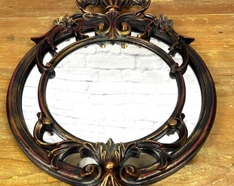 May include: Ornate oval mirror with a gold and red painted frame. The frame has a detailed, intricate design with a floral motif. The mirror is perfect for adding a touch of elegance to any room.