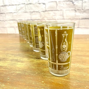 May include: Set of six clear glass tumblers with a gold and white pattern. The pattern features a variety of images, including a duck, a lamp, a gun, and a candlestick.