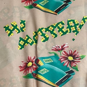 May include: A repeating pattern on a light tan fabric. The design features teal books with "HIS" on them, red flowers, and the words "HI" and "ANNIVERSARY" in a green and yellow plaid pattern.
