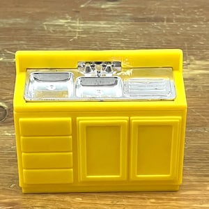 May include: A bright yellow toy kitchen sink and cabinet set. The sink has a silver faucet and basin, with a drainboard. The cabinet has two doors and three drawers. The toy is made of plastic.
