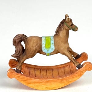 Op de afbeelding: Een bruin schommelpaard met een blauw en groen zadel. Het paard staat op een houten schommelbasis.