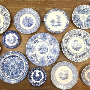 May include: A collection of twelve ceramic plates and saucers featuring blue and white transferware patterns. The pieces display various landscape, floral, and geometric designs with scalloped or smooth edges, arranged in a flat layout.