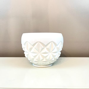 May include: A white ceramic bowl with a diamond-shaped pattern. The bowl is sitting on a white surface.