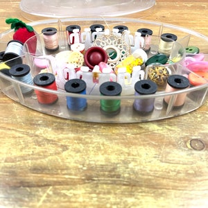 May include: A clear plastic sewing box with multiple compartments filled with spools of thread in various colors, buttons, and other sewing notions.