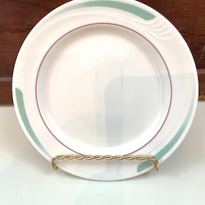 May include: A white ceramic plate with a green and burgundy rim. The plate has a simple design with a subtle wave pattern.
