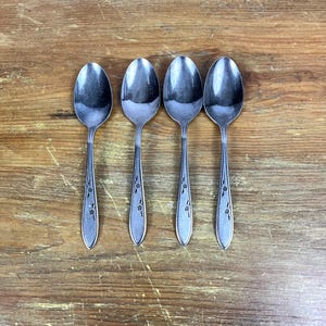 Puede incluir: Cuatro cucharas de plata con diseños florales sobre una superficie de madera.