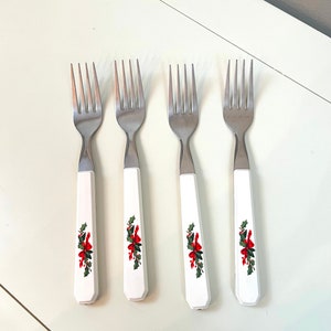 May include: Set of four silver forks with white handles featuring a red and green holly and bow design.