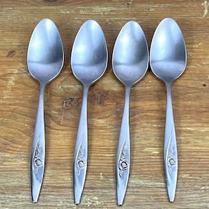 May include: Four stainless steel spoons with a floral design on the handles. The spoons are arranged on a wooden surface. The spoons have a classic, elegant design, suitable for everyday use or special occasions.
