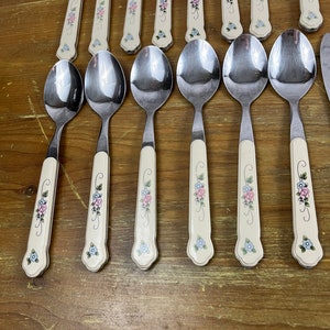 May include: A set of 12 stainless steel spoons with floral patterned handles. The handles are cream colored with pink and blue flowers.