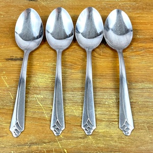 May include: Four silver spoons with a decorative design on the handle. The spoons are arranged in a row on a wooden surface.