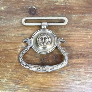 Puede incluir: Pomo de puerta de plata con una cabeza de león en el centro y dos pájaros estilizados a cada lado. El pomo está marcado con "Inglaterra".