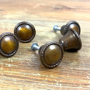 May include: Four antique-style cabinet knobs with a brown finish and a decorative rim. The knobs have a slightly raised center and are attached to silver screws.