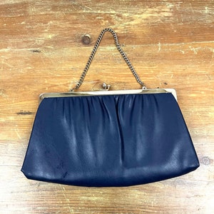 May include: A navy blue leather clutch purse with a silver chain strap.