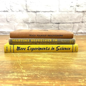 May include: A stack of three vintage books with titles visible: "Teach Yourself Trigonometry," "Wartime Refresher in Fundamental Mathematics," and "More Experiments in Science." The books are in shades of brown, green, and yellow, stacked on a wooden surface.