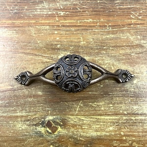 May include: A decorative cast iron drawer pull with a circular, ornate design. The pull has a dark brown finish and features a floral pattern.