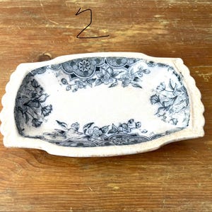 May include: A rectangular, cream-coloured ceramic dish with a scalloped edge. It has a floral pattern in blue and grey. The number "2" is written in black marker in the upper left corner.