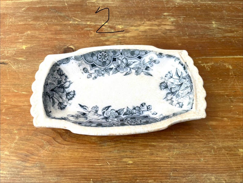May include: A rectangular, cream-coloured ceramic dish with a scalloped edge. It has a floral pattern in blue and grey. The number "2" is written in black marker in the upper left corner.