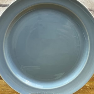 Puede incluir: Un plato redondo de cerámica azul claro con un borde ancho. El plato tiene un acabado liso y brillante y es adecuado para servir alimentos. El plato tiene aproximadamente 30 cm de diámetro.